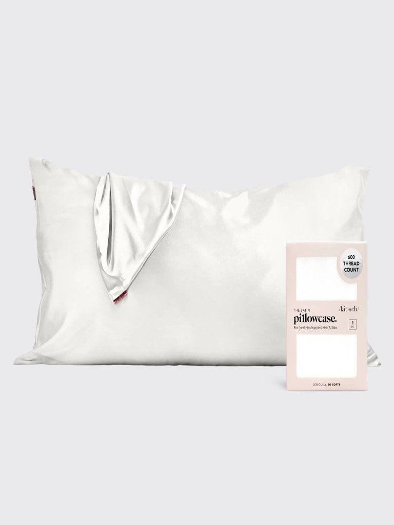 A king-size white satin pillowcase displayed on a bed with its packaging in the foreground.