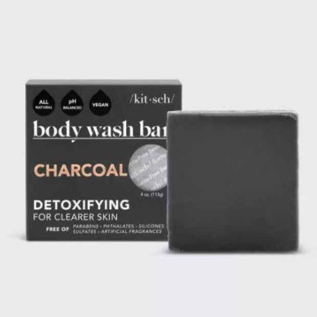 A black bar of charcoal detoxifying body wash, with a box packaging in the background that reads 'Charcoal' and 'Detoxifying for Clearer Skin'. The product is identified as being free of sulfates, parabens, and artificial fragrances.